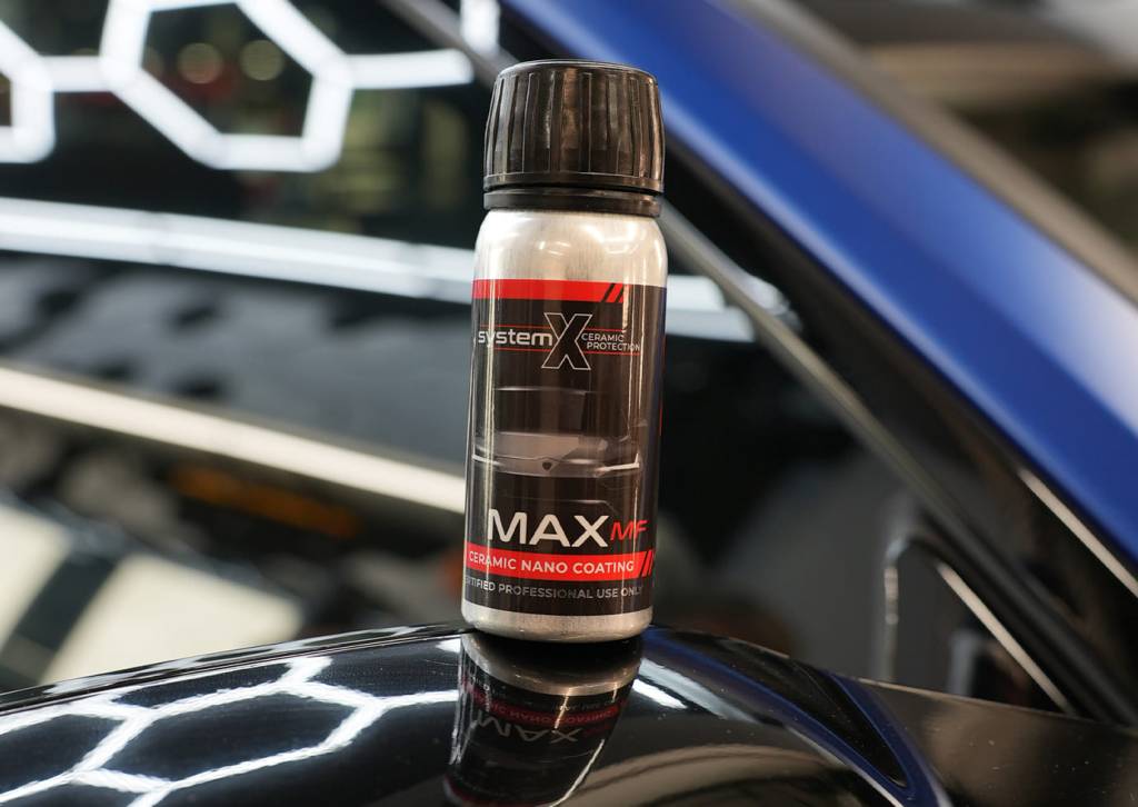 Modern car driving through Brooklyn with System X Ceramic Coating, reflecting sunlight and street scenery on flawless paintwork